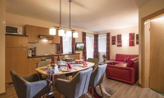 A modern living room with an open kitchen and a dining area. The space has neutral tones and cozy furniture.