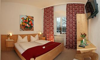 A cozy bedroom with a large bed and red accents. The room is bright and inviting, with a small table and a television.