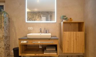 A modern bathroom with an elegant sink on a wooden cabinet. On the wall, there is a lit mirror and a space-saving cabinet.