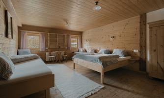A cozy room with wooden walls and two single beds. There is a small table and chairs, which stand in a warm, inviting atmosphere.