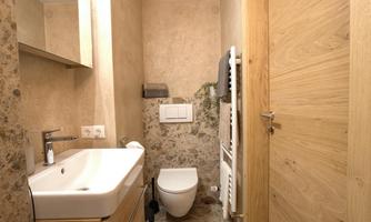 A modern bathroom with a sink and a toilet. The walls are designed in neutral colors, and there are some decorative wooden elements.