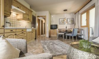 A cozy living kitchen with wooden cabinets and a dining table. Large windows provide plenty of daylight and create an inviting atmosphere.