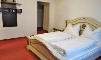 A cozy bedroom with a large double bed and two large pillows. The floor is red and there is a shelf hanging on the wall.