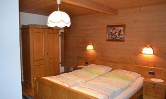 A cozy bedroom with wood paneling and a double bed. The walls are colorfully decorated, and a beautiful wardrobe complements the space.