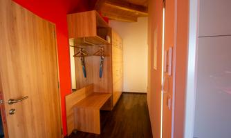A modern hallway with wooden paneling and red walls. There is a wardrobe with coat hooks and a seating area.