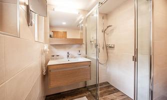 A modern bathroom with a glass shower cabin and a stylish sink. The design is bright and friendly with wooden and tiled accents.