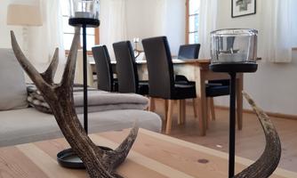 A decorative antler stand with candle holders on a wooden table. In the background, an elegant dining room can be seen.