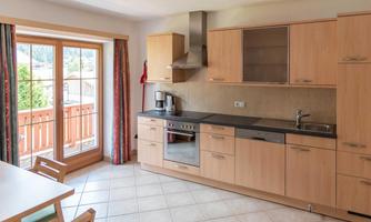 A modern kitchen with bright wooden cabinets and a cooking area. Large windows provide plenty of daylight and a view outside.