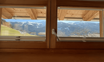 A view from a window of a mountainous landscape. In the background, snow-capped mountains and a blue sky are visible.