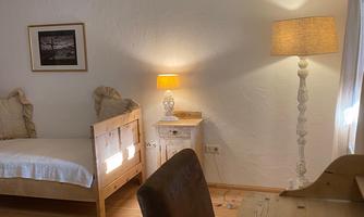 A cozy bedroom with a bed, a workspace, and a light. The walls are bright and the wooden details create a warm atmosphere.