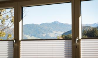 A glance through a window at a picturesque mountain landscape. The sun is shining and there is a clear sky visible.