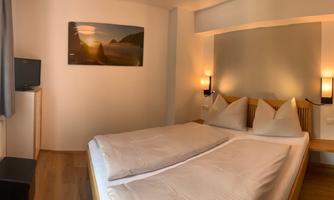 A comfortable bedroom with a large double bed and modern amenities. The room is bright and inviting, with a television and a picture on the wall.