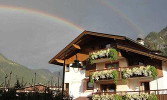 A beautiful half-timbered house with flower balconies and a rainbow in the background. The landscape is surrounded by mountains and appears picturesque.