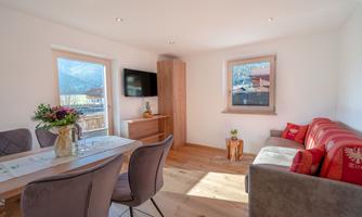 A bright and modern living room with a cozy sofa and a dining table. Large windows offer a beautiful view of the surrounding nature.
