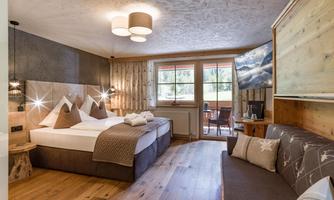 Bright and cozy hotel room with a double bed and modern decor. Large windows provide a view outside and there is a seating area with a TV.
