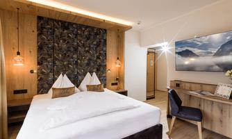 A modern hotel room with a large bed and elegant wooden paneling. A television hangs on the wall and there is a small desk.