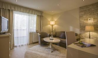 A modern living room with a comfortable sofa, a coffee table, and a TV. Large windows provide plenty of daylight and a pleasant atmosphere.