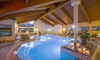 An elegant indoor pool with a wooden ceiling and soft lighting. There are cozy loungers and plants that create a relaxed atmosphere.