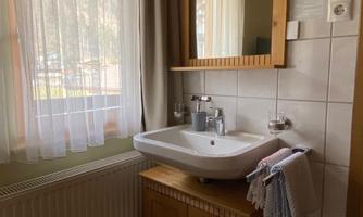 A simple bathroom with a sink and a large mirror. The windows let in plenty of daylight.