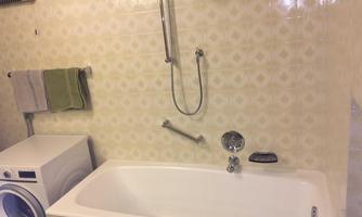 A bathroom with a white bathtub and a shower fixture. Next to the bathtub is a washing machine and two towels are hanging on the wall.