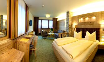 A cozy hotel room with wooden accents and a large window. It is modernly furnished with two beds, a table, and a comfortable armchair.