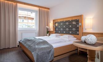 A modern bedroom with a comfortable double bed and elegant wooden decor. Large windows provide plenty of light and a cozy atmosphere.