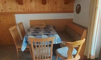 A cozy dining area with a wooden table and chairs. The walls are clad with wood panels, and a large window lets in plenty of light.