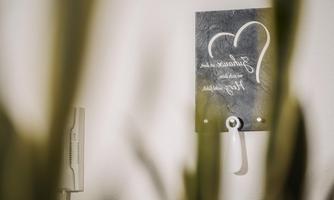 A heart made of stone with a handwritten message hangs on the wall. In the foreground, green plants can be seen.