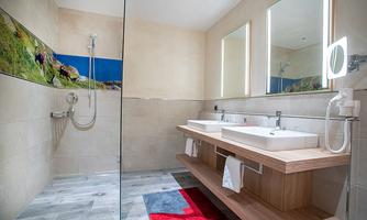 A modern bathroom with a glass shower and two sinks. The floor is decorated with gray tiles and a colorful rug.