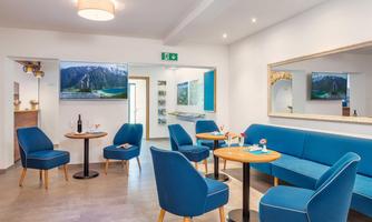 A modern lounge with blue furniture and small tables. Large pictures are on the walls, and the atmosphere is inviting and friendly.