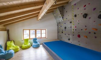 A modern room with a climbing wall and comfortable bean bags in bright colors. The floor is covered with a blue mat, perfect for safe climbing.