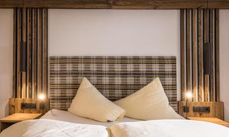 A cozy bed with a checked headboard and two large pillows. The wooden paneling and the stylish bedside lamps give the room a warm atmosphere.