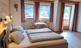 A cozy bedroom with a double bed and wooden elements. Large windows offer views of the surroundings and let in a lot of light.