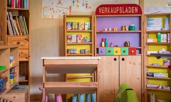 A small sales booth with colorful shelves and toy packaging. On a table are colorful chairs and a creative space for children.