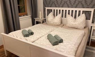 A cozy bedroom with a double bed and decorative pillows. On the bedspread, there are green towels, and the walls are designed with a contemporary pattern.