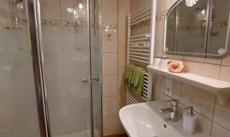 A modern bathroom with a shower and a sink. The walls are light tiled and there is a green towel holder.