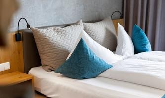 A cozy bedroom with a large bed and soft pillows. The walls are painted in soft tones, and a nightstand complements the modern design.