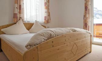 A bright bedroom with a large wooden bed and two pillows. Large windows provide a view outside.