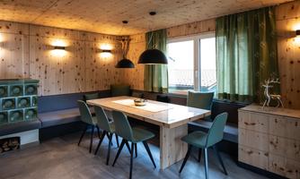 A modern dining room with wood paneling and a large window front. The table is made of light wood, surrounded by elegant chairs and stylish lighting.