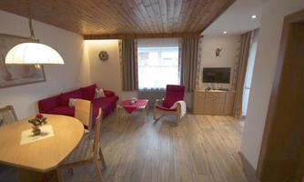 A cozy living room with a red sofa and a wooden dining table. Large windows let in plenty of light.
