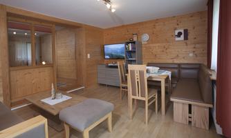 A cozy living atmosphere with wooden walls and a modern television. The room is equipped with a dining area and a seating corner.