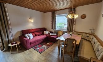 A cozy living room with a red couch and a dining area. Large windows let in plenty of light and give the room an inviting atmosphere.