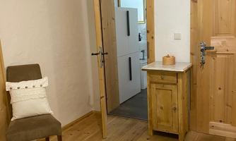 A cozy room with wooden furniture and a carpet. An open door leads to another room with modern elements.