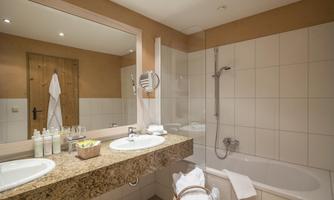 A modern bathroom with double sinks, a shower area, and a bathtub. Bright tiles and a pleasant atmosphere create an inviting environment.