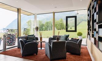 A modern living room with cozy seating and a view of the green landscape. Large windows provide plenty of daylight.