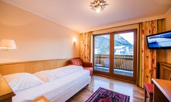 A cozy hotel room with a double bed and a single bed. Large windows provide a view of the mountains, and the room is bright and cheerfully furnished.