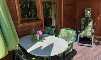 A cozy outdoor area with a round table and colorful chairs. In the background, there is a rocking chair and there is a green awning.