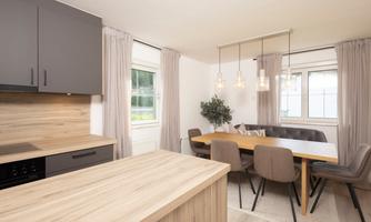 A modern kitchen with a wooden work surface and elegant furniture. The dining area is bright and welcoming with a large table and comfortable chairs.