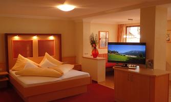 A cozy bedroom with a double bed and large pillows. There is a television and bright lighting that enhances the pleasant atmosphere.