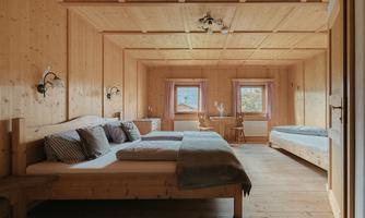 A cozy room with wood paneling and two beds. The windows offer a view of the outdoors and the light creates an inviting atmosphere.